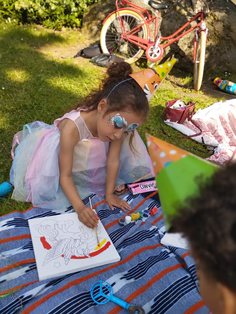 Petite fille maquillée en train de colorier lors d'un anniversaire en plein air